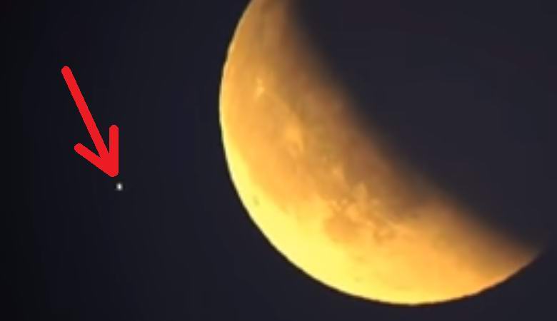 Un UFO lampeggiante che vola contro una luna rossa